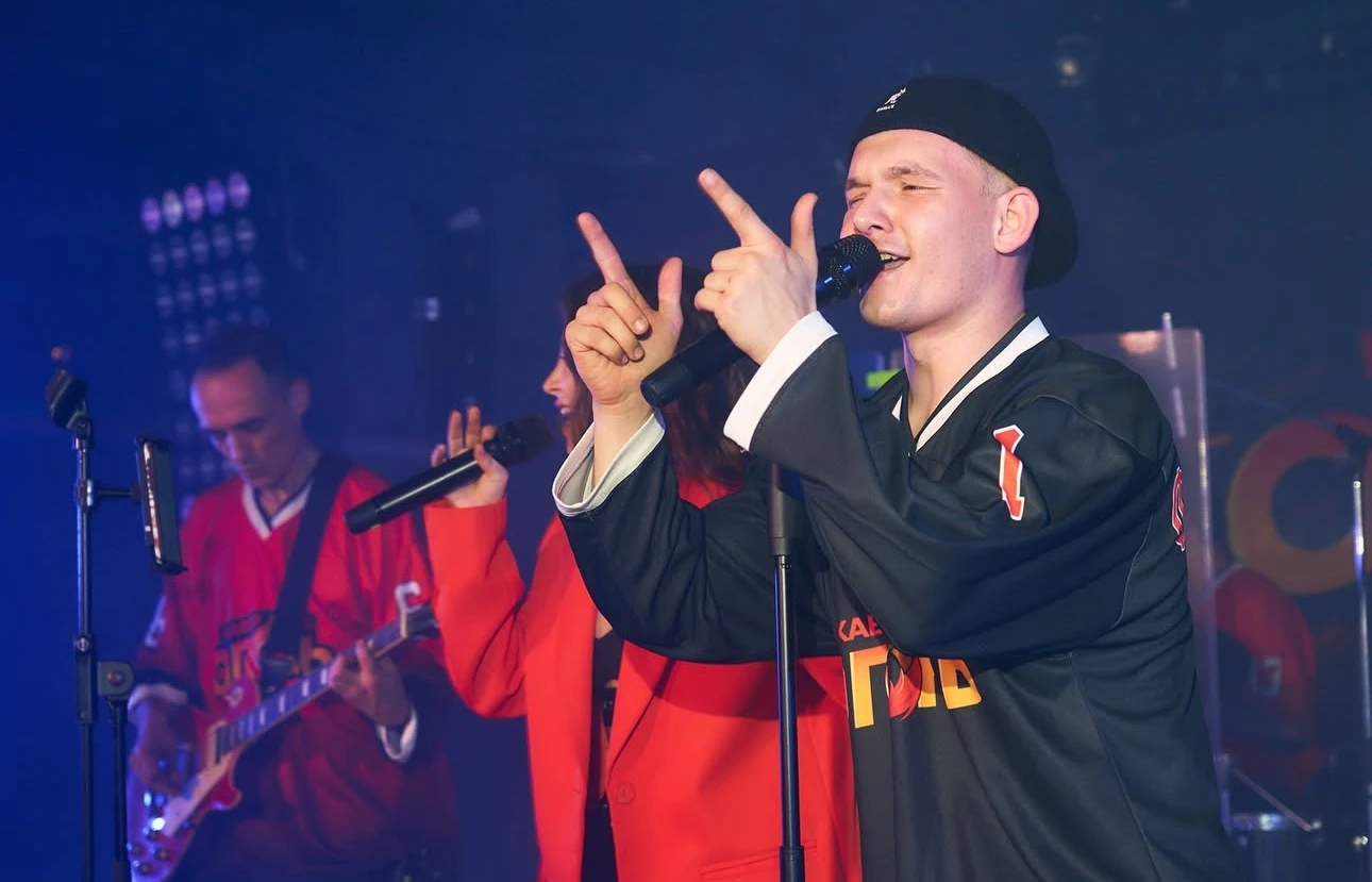 солист кавер-группы в джерси поёт на сцене под синей подсветкой с микрофоном