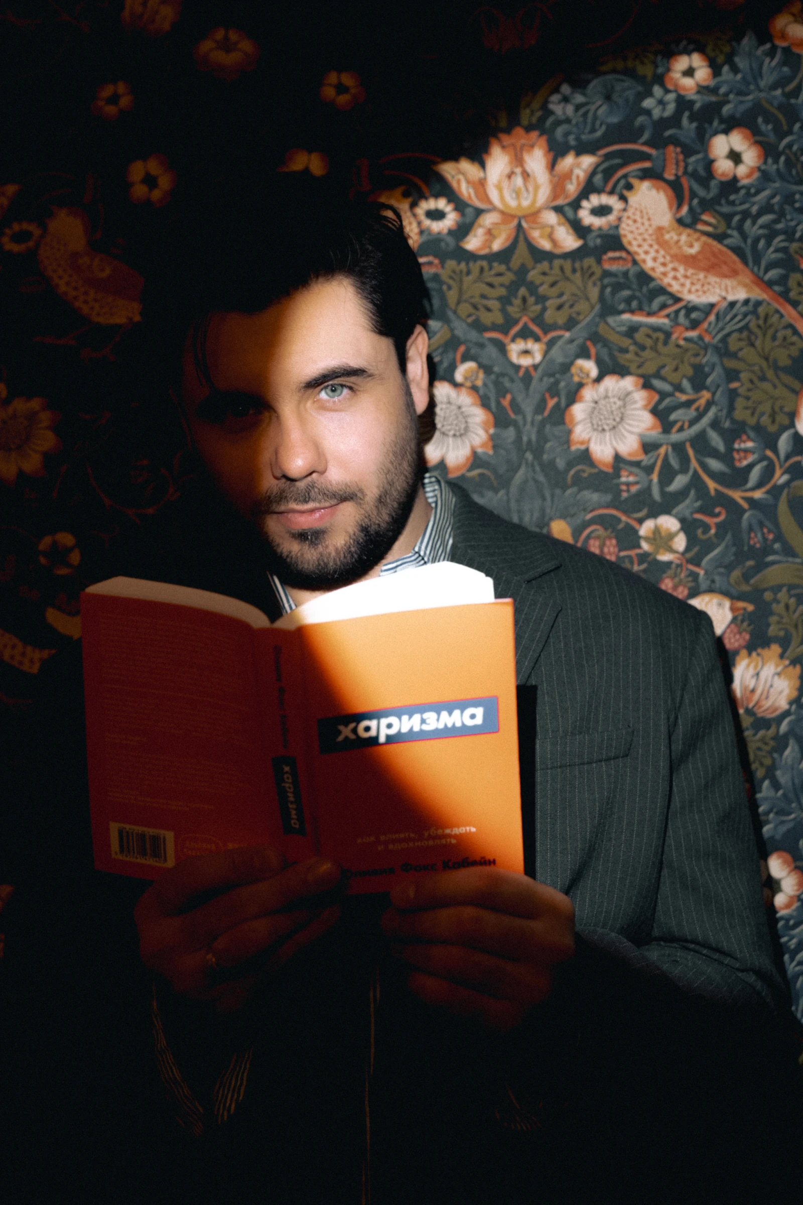 портрет ведущего в пиджаке с книгой на фоне цветочных обоев