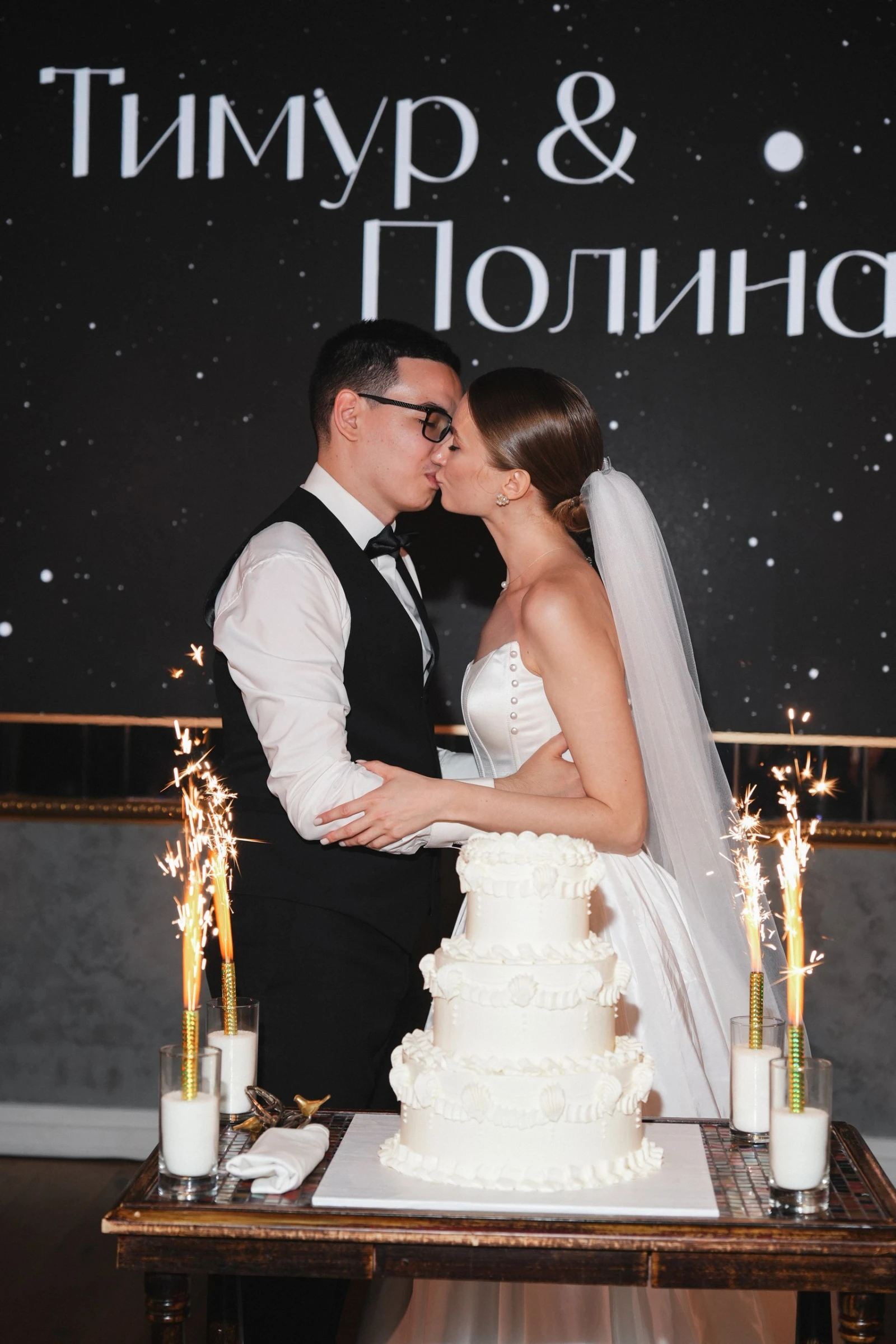 молодожёны целуются у трёхъярусного торта с бенгальскими огнями в банкетном зале