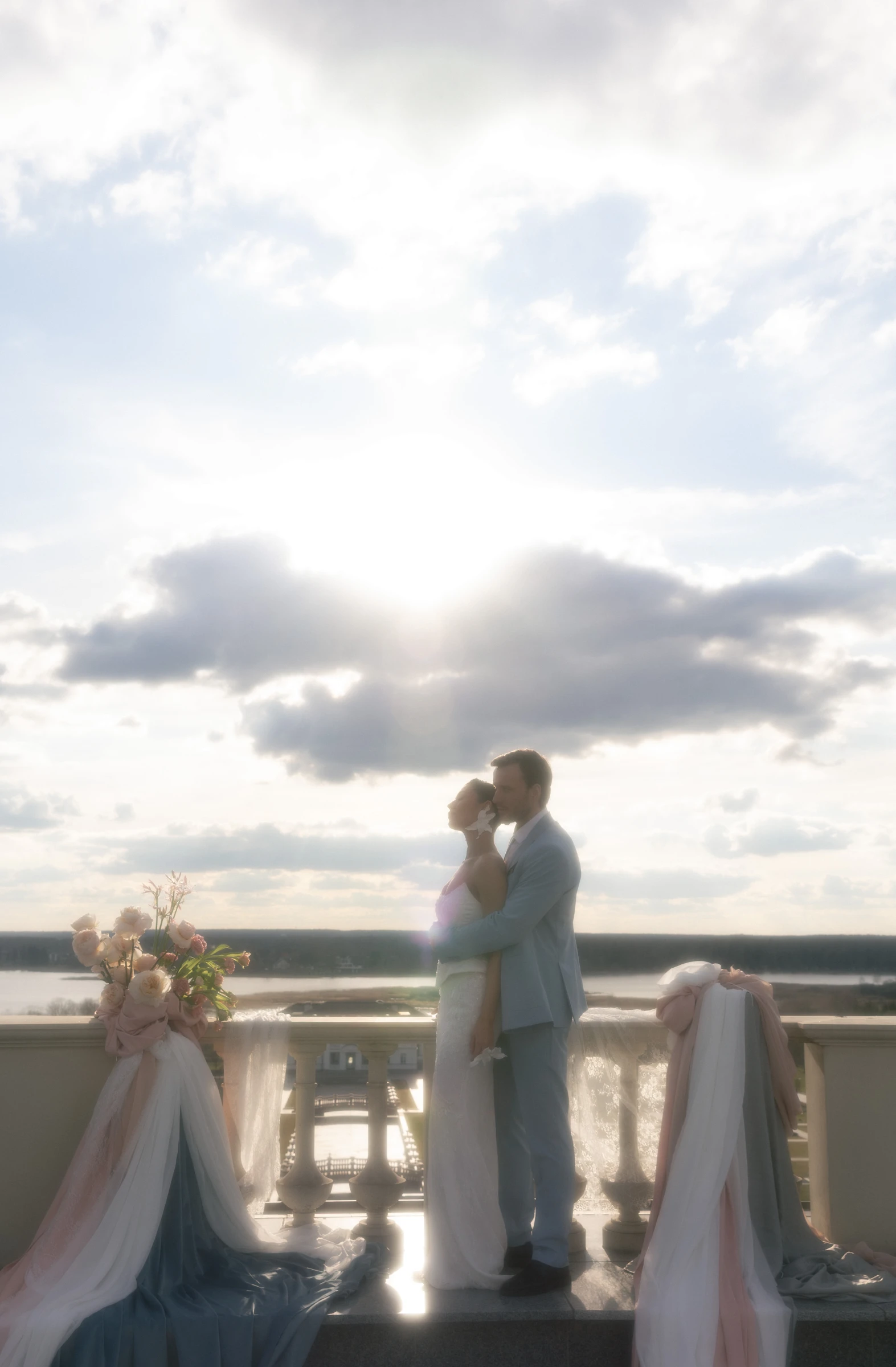 жених и невеста целуются на балконе с видом на реку и текстильным декором