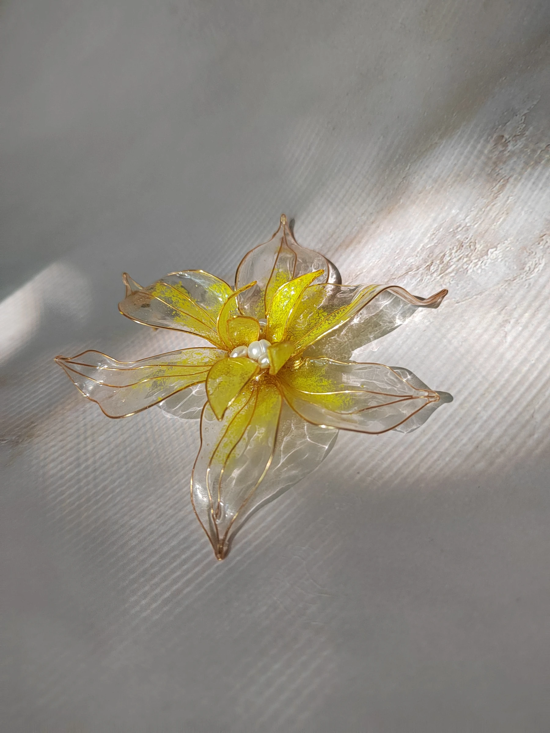 прозрачная брошь-цветок с жёлтым напылением и жемчужной серединкой на ткани