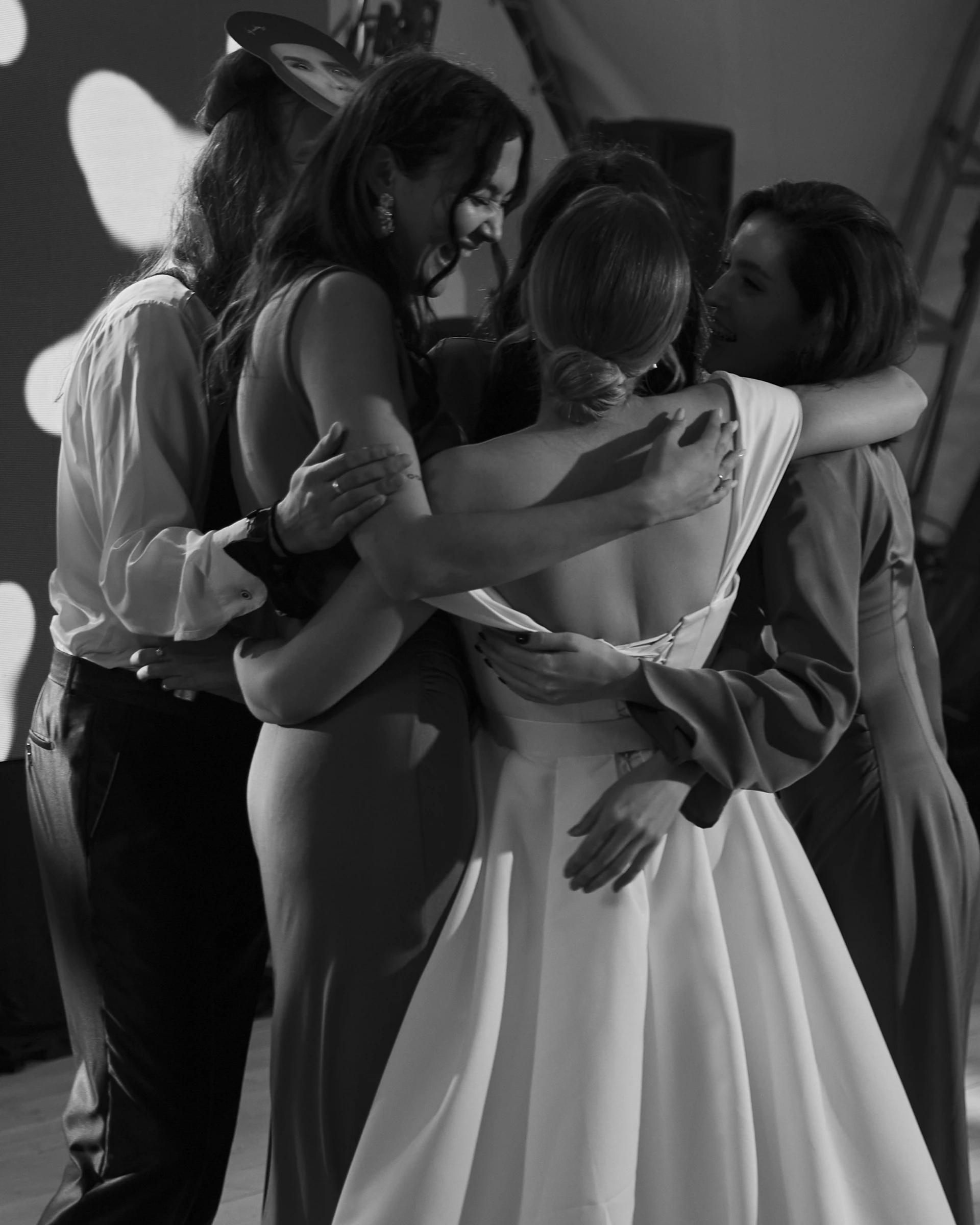 Невеста в атласном платье обнимается с подружками в лучах прожектора
