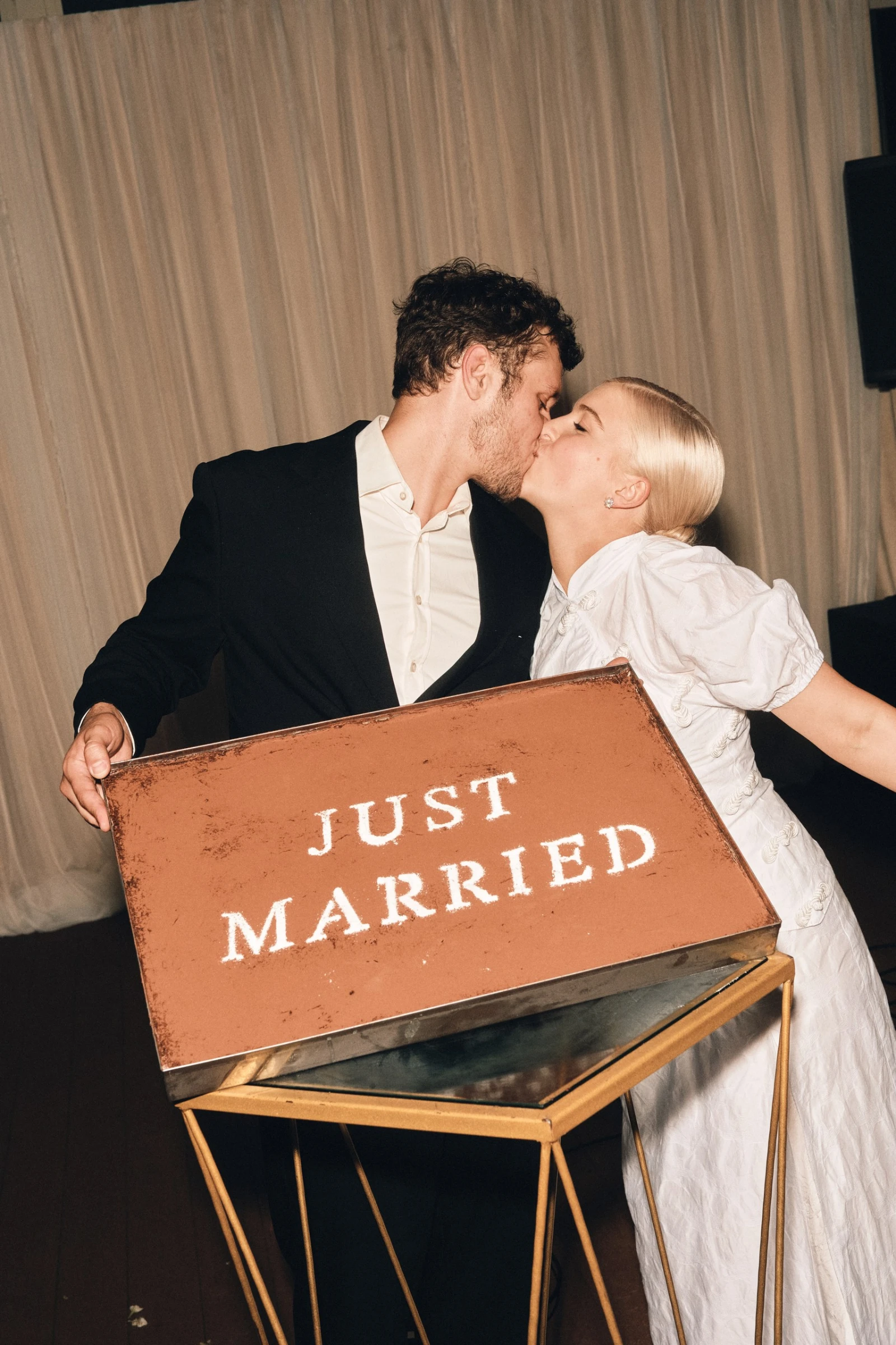 молодожёны целуются за табличкой Just Married на вечернем приёме