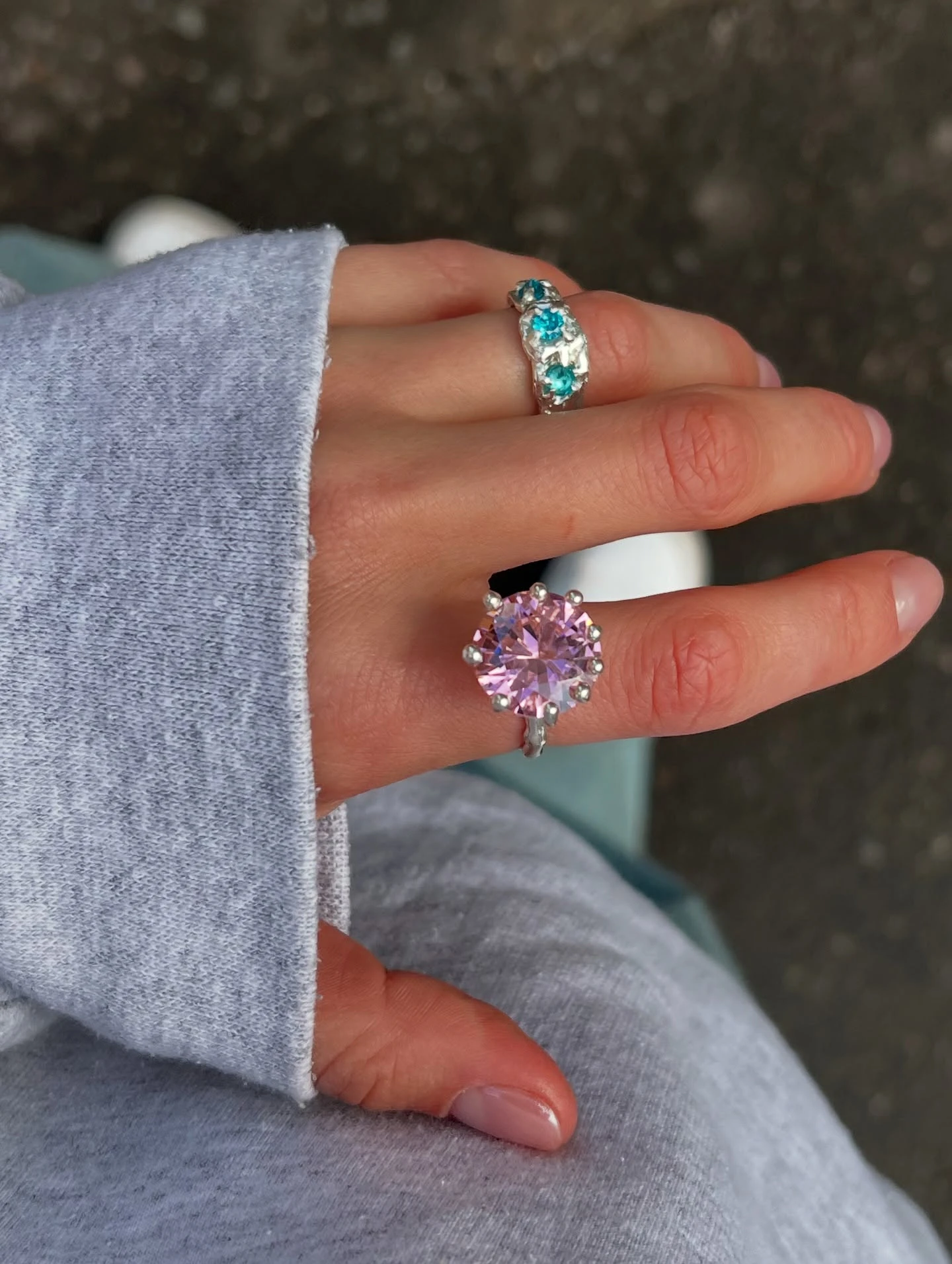 серебряные кольца с розовым и голубыми камнями на руке рядом с фотоаппаратом