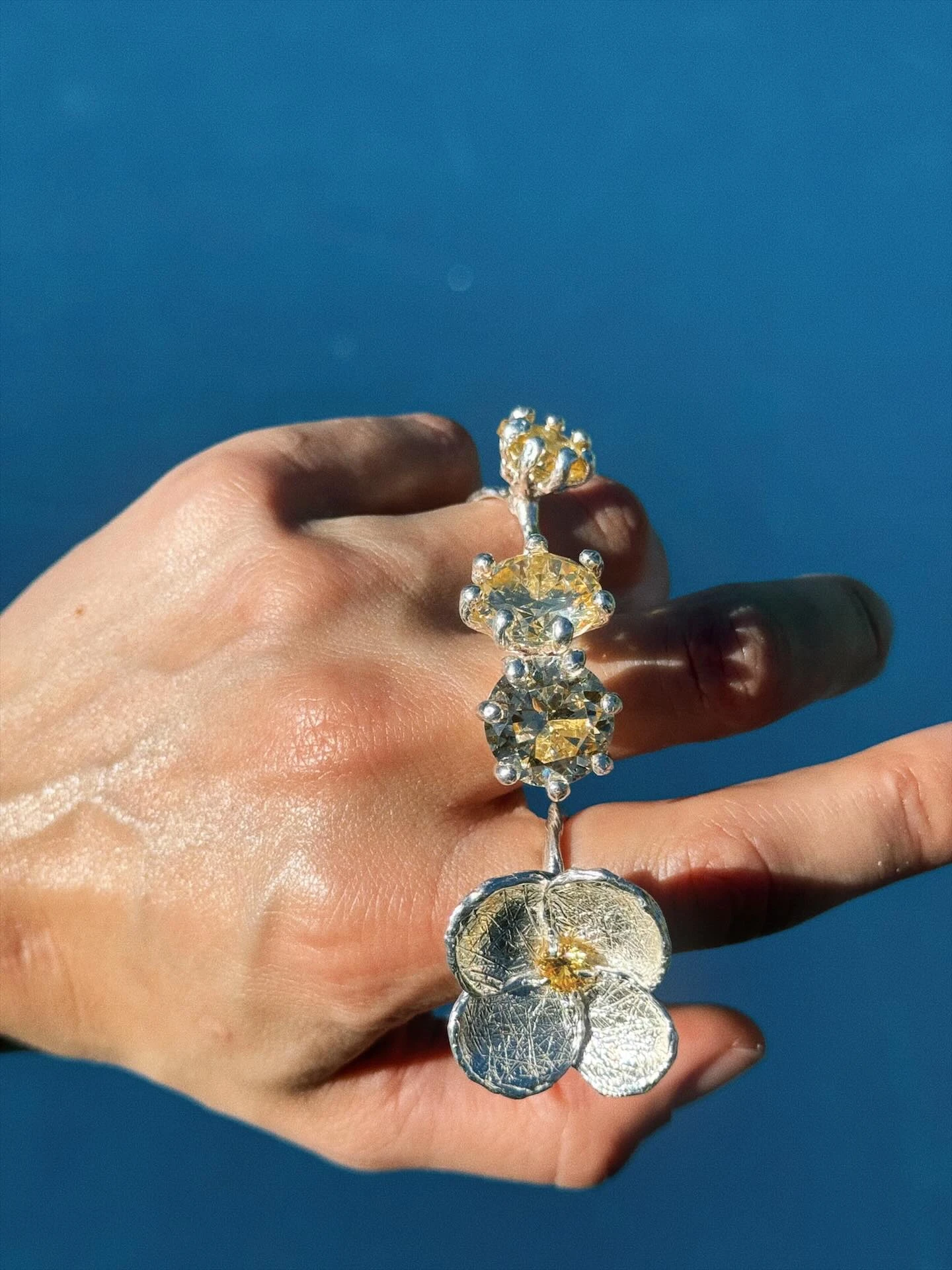 каскадное серебряное кольцо с жёлтыми камнями и цветком на руке у воды