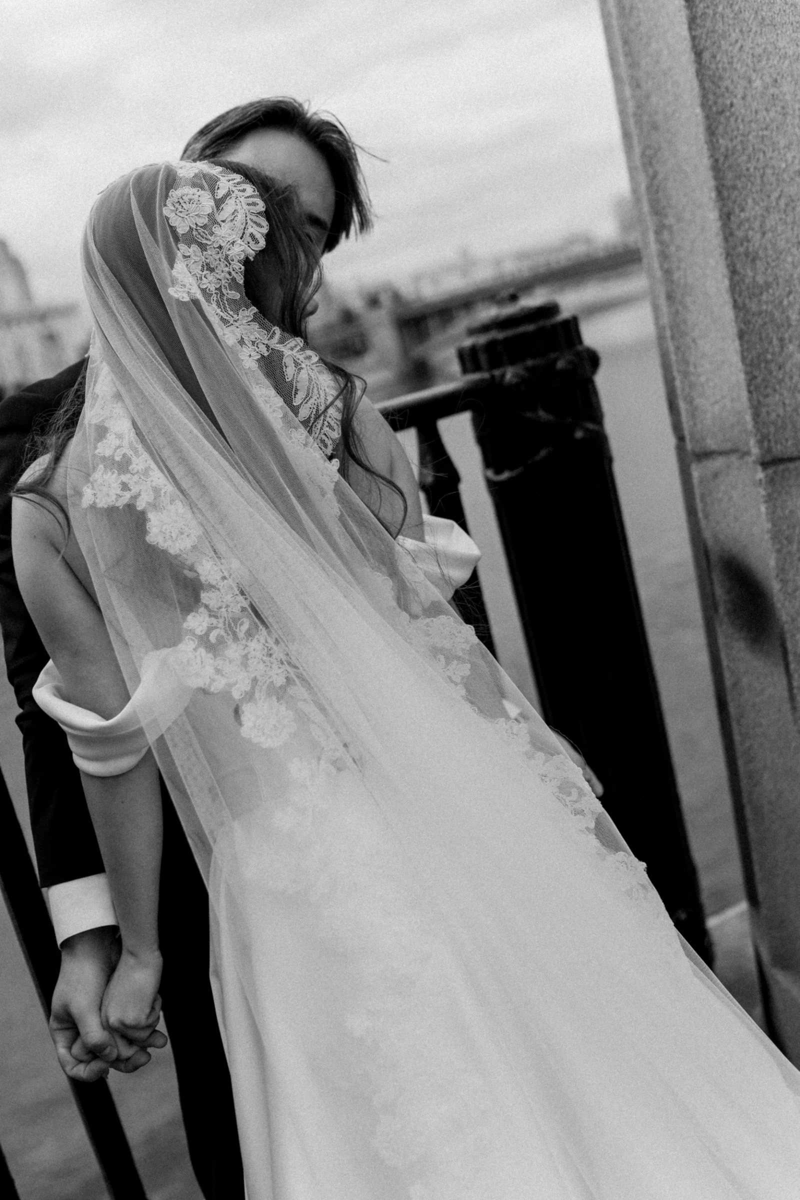 невеста в кружевной фате держит жениха за руку на набережной