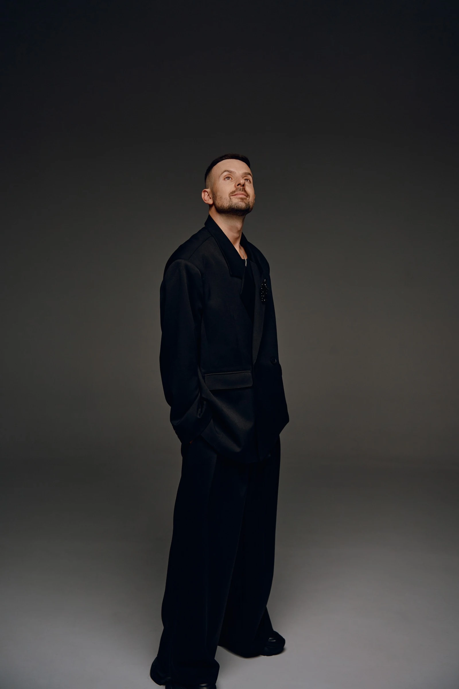 портрет ведущего в полный рост в тёмном костюме с брошью