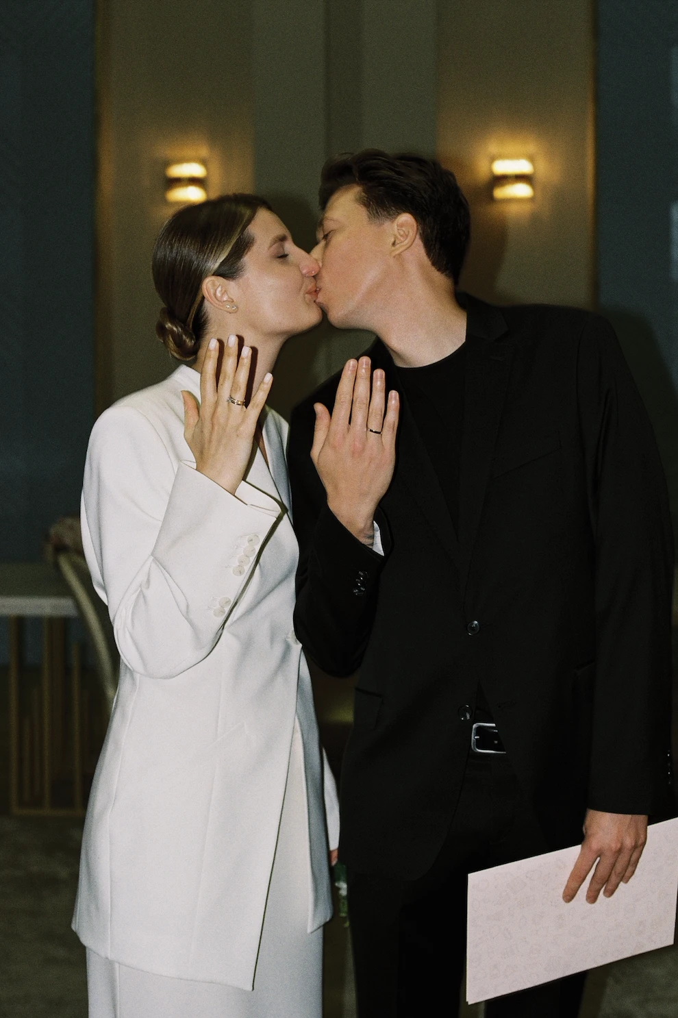поцелуй жениха и невесты с обручальными кольцами на фоне тёплого света