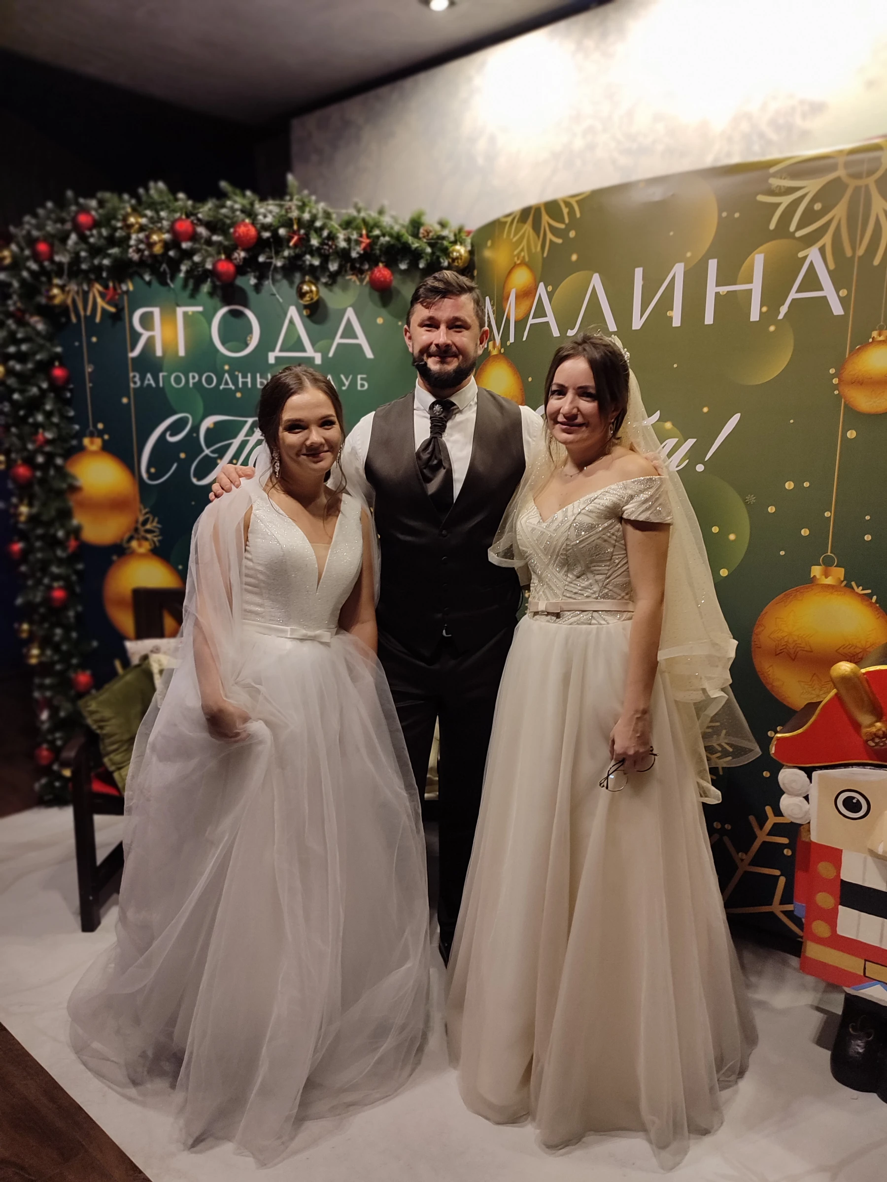ведущий с двумя невестами в платьях у новогодней фотозоны