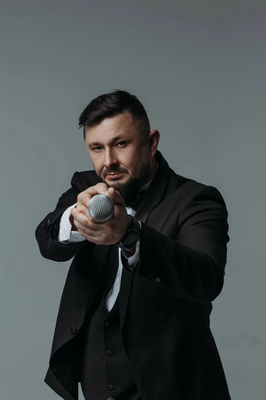 ведущий протягивает микрофон в объектив на сером фоне
