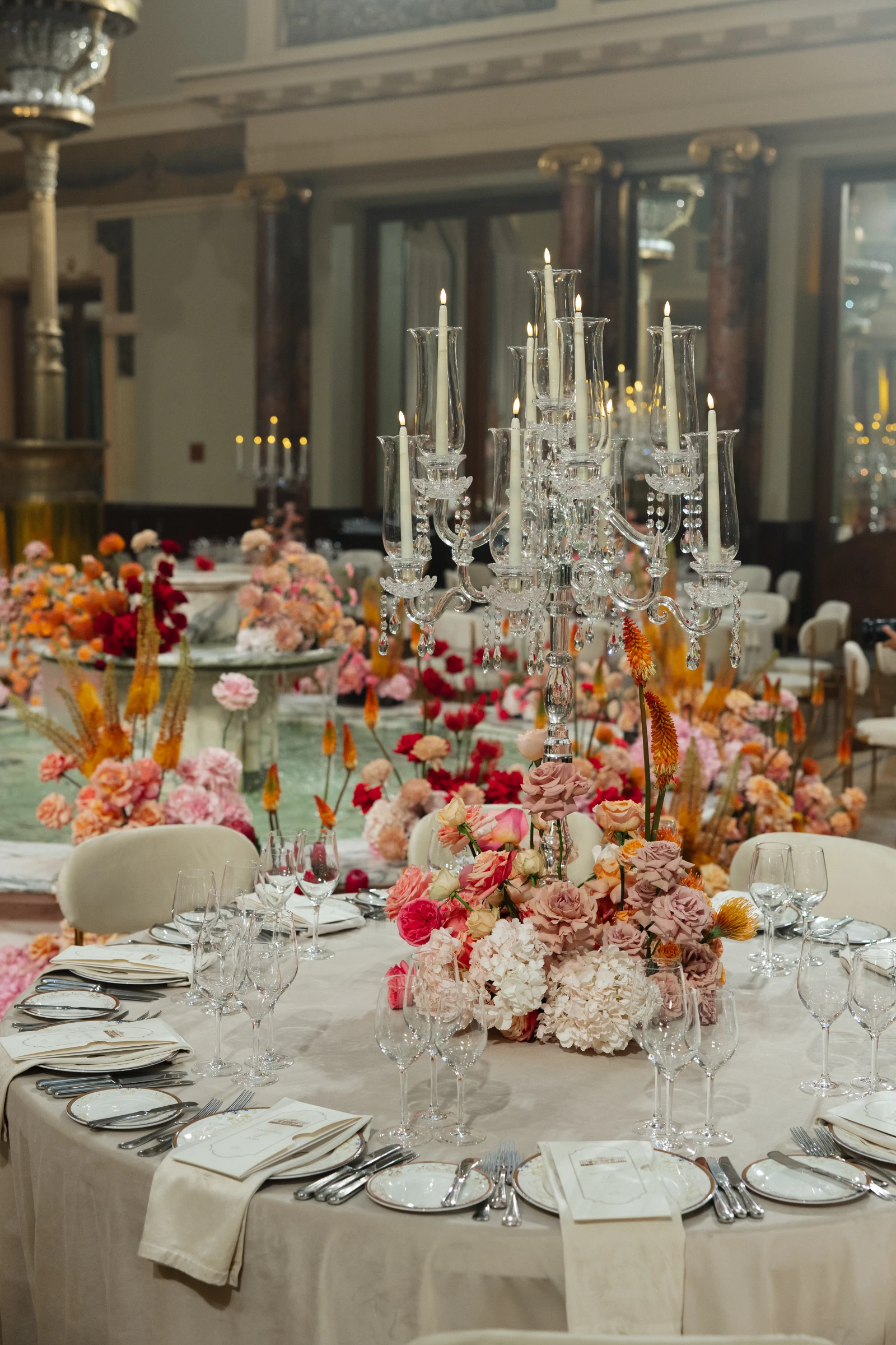 Хрустальный канделябр со свечами в розово-оранжевой цветочной композиции на банкетном столе
