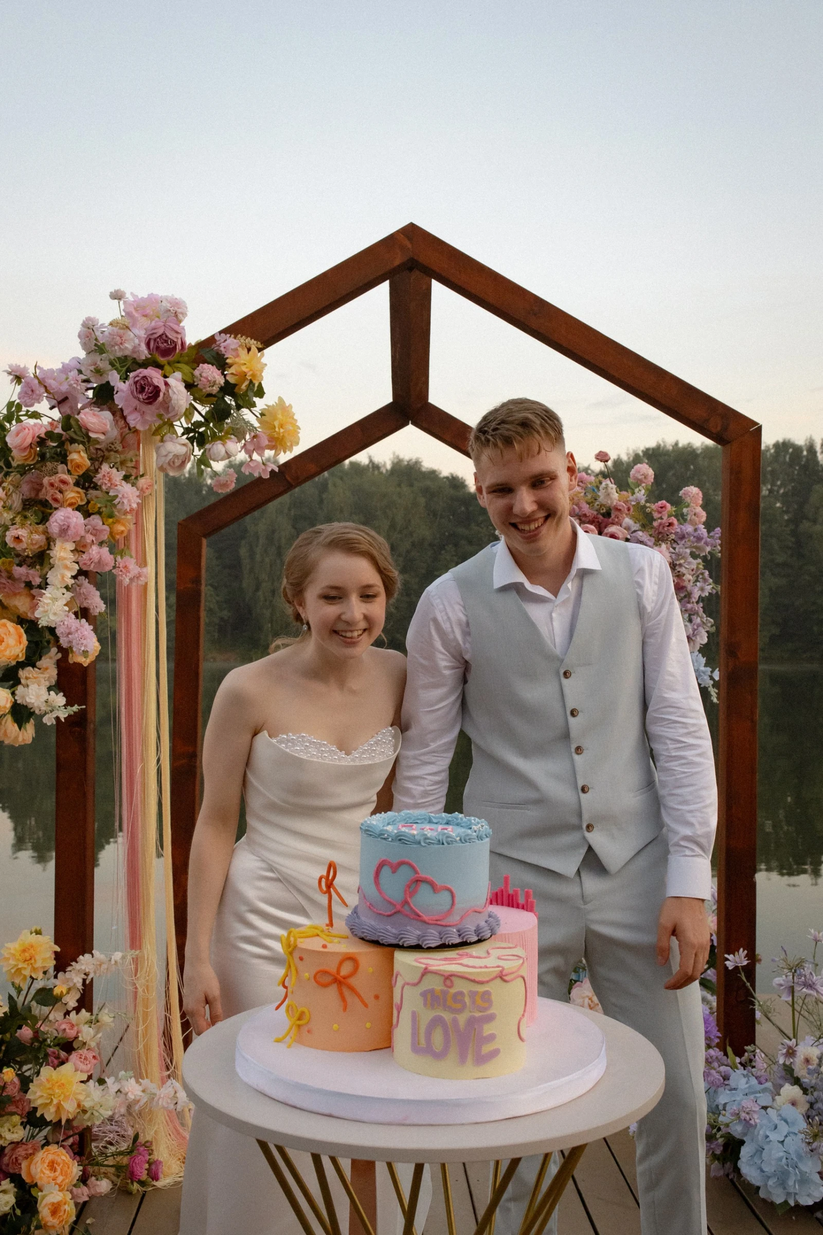 разноцветный трёхъярусный свадебный торт с надписью this is love у озера