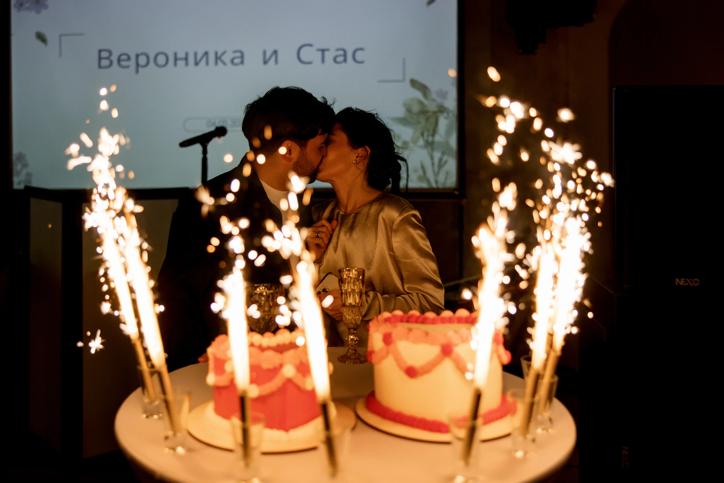 пара целуется у праздничных тортов с бенгальскими огнями на банкете