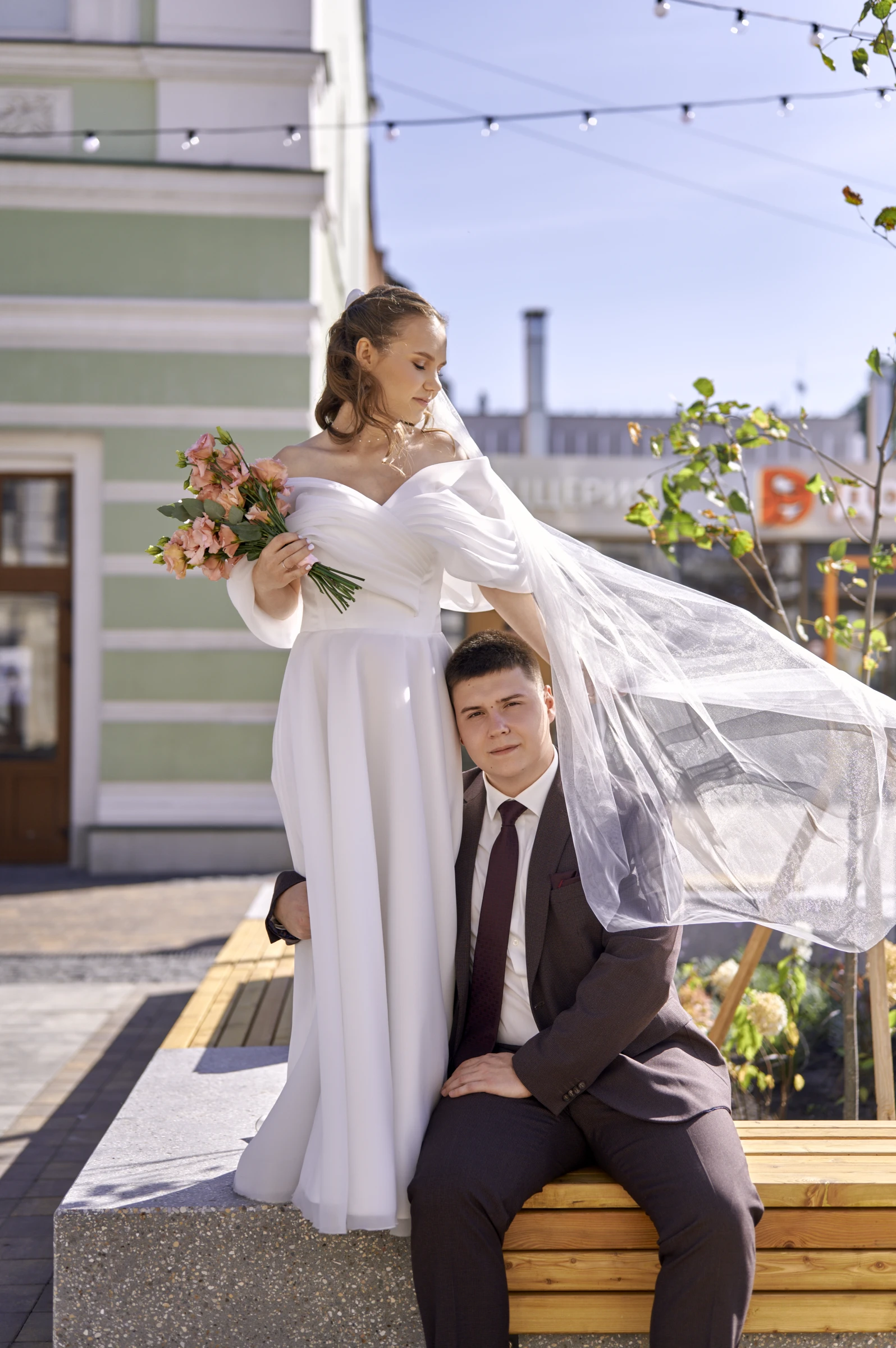 невеста с летящей фатой обнимает жениха на каменной скамье