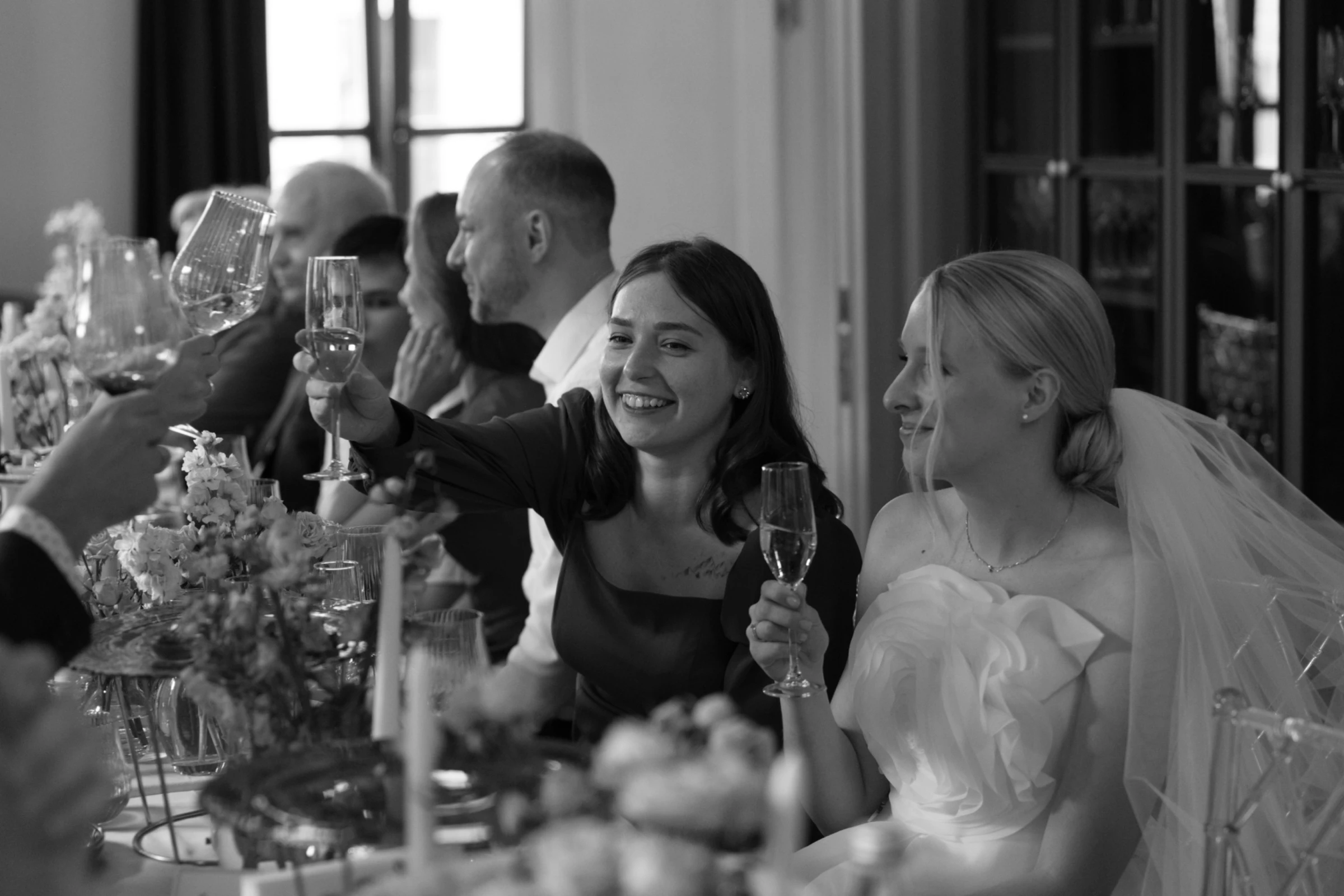 гости поднимают бокалы шампанского за невесту в фате на свадебном банкете