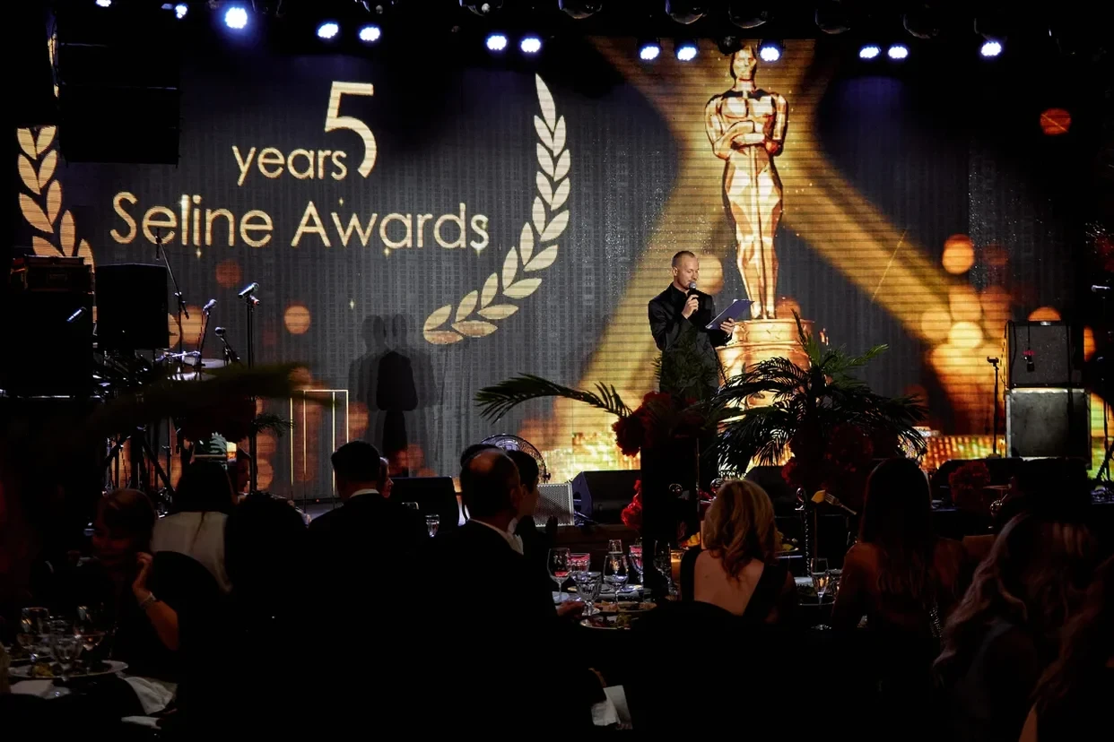 ведущий с микрофоном на сцене премии Seline Awards среди гостей за столами