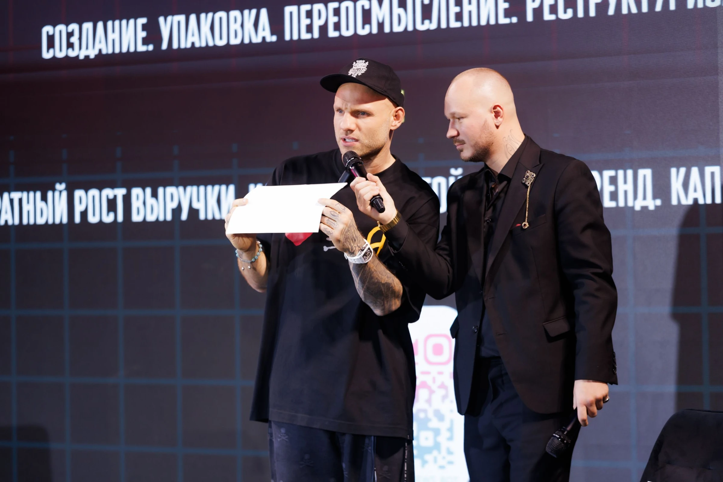 ведущий с конвертом и микрофоном на сцене бизнес-конференции рядом с партнёром
