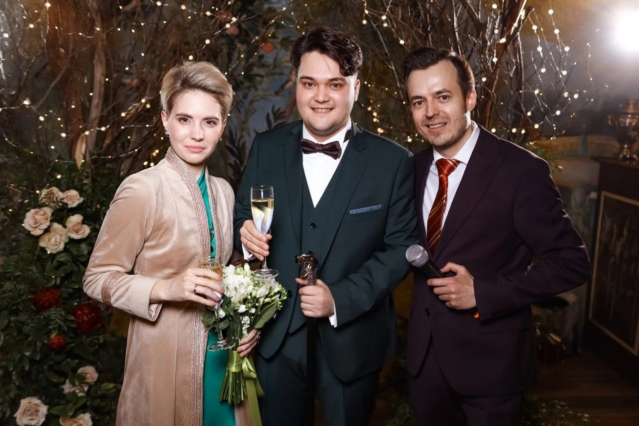 ведущий с женихом и невестой на фоне цветочного декора и гирлянд