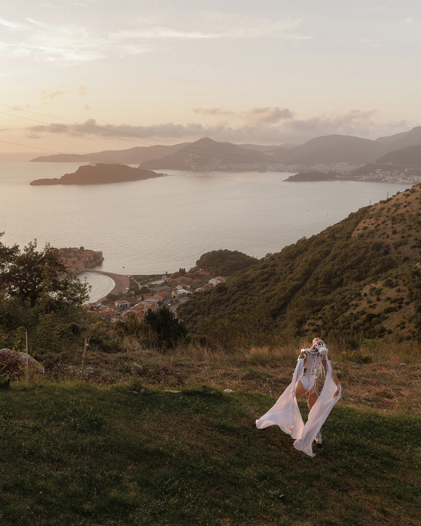 невеста в белом наряде на холме с видом на бухту и острова на закате
