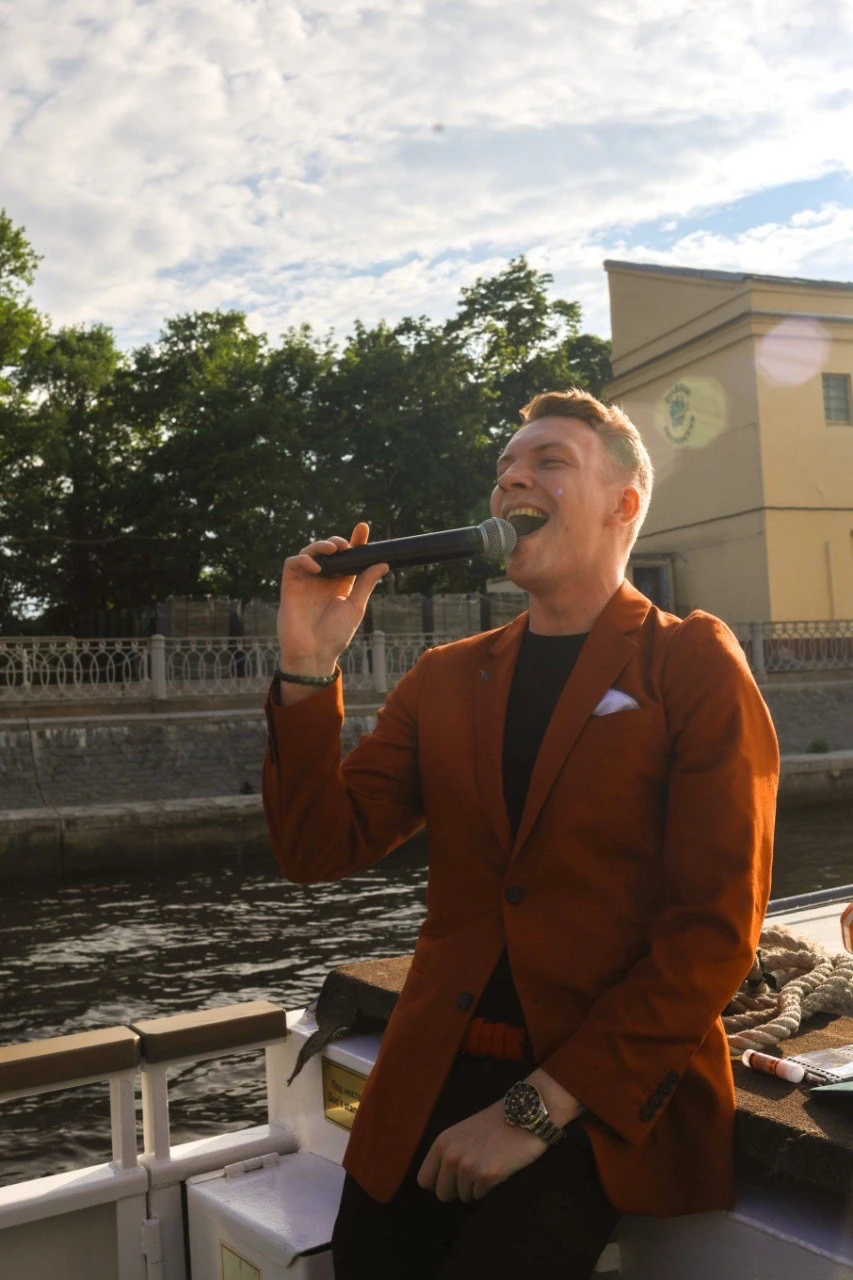 ведущий в терракотовом пиджаке поёт в микрофон на палубе теплохода