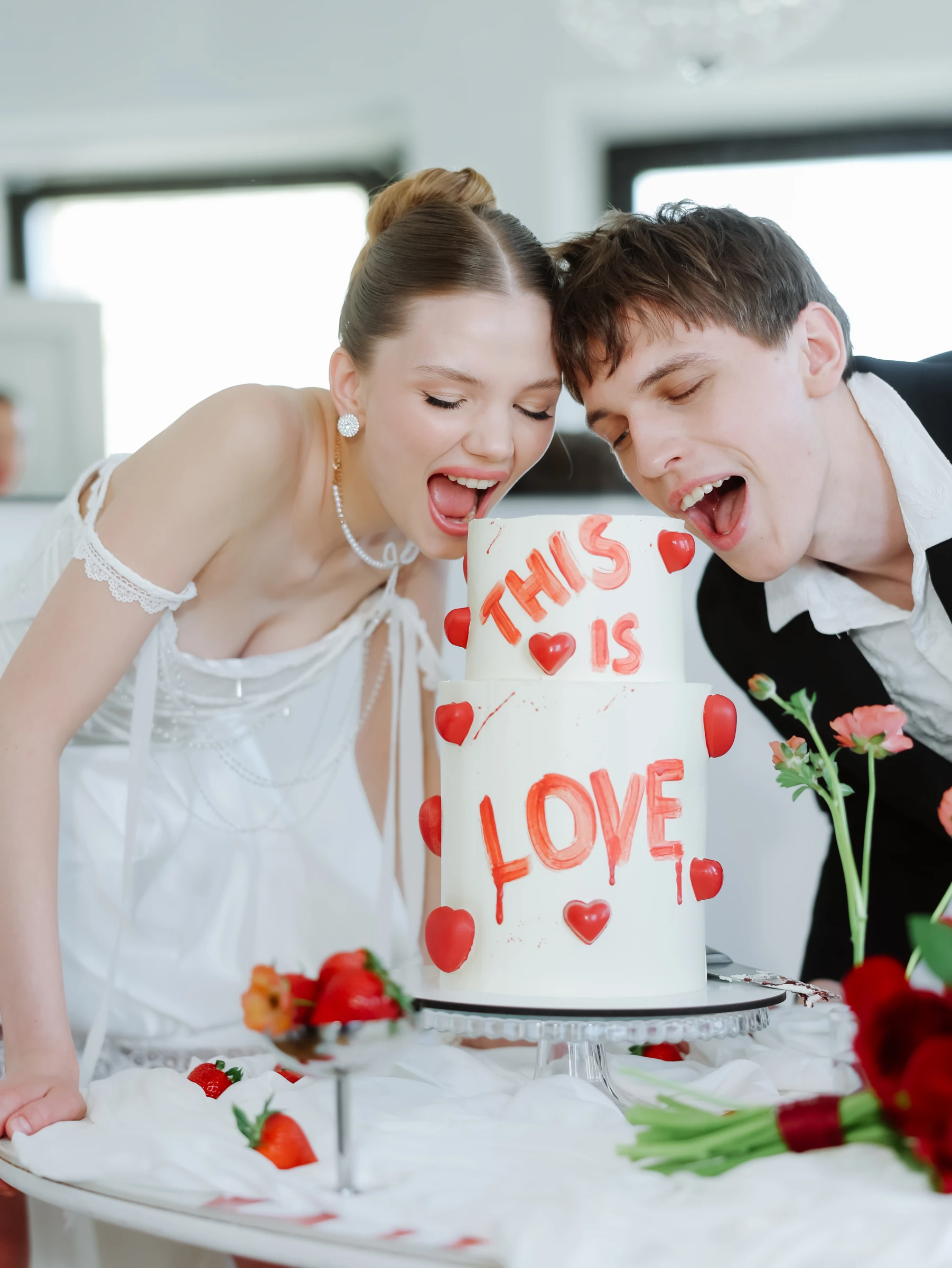 молодожёны кусают свадебный торт с надписью This is Love