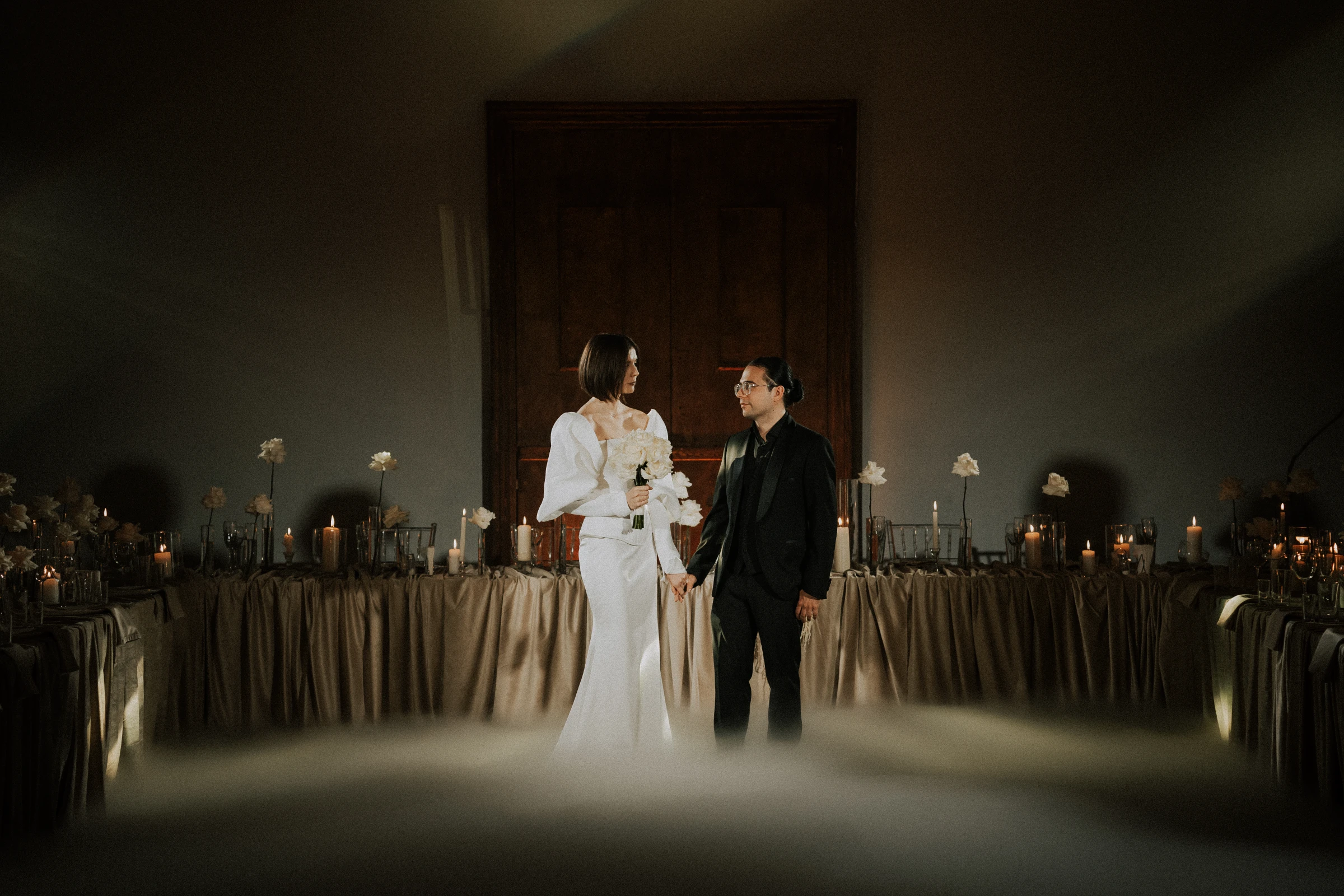 невеста и жених держатся за руки среди свечей на банкетном столе