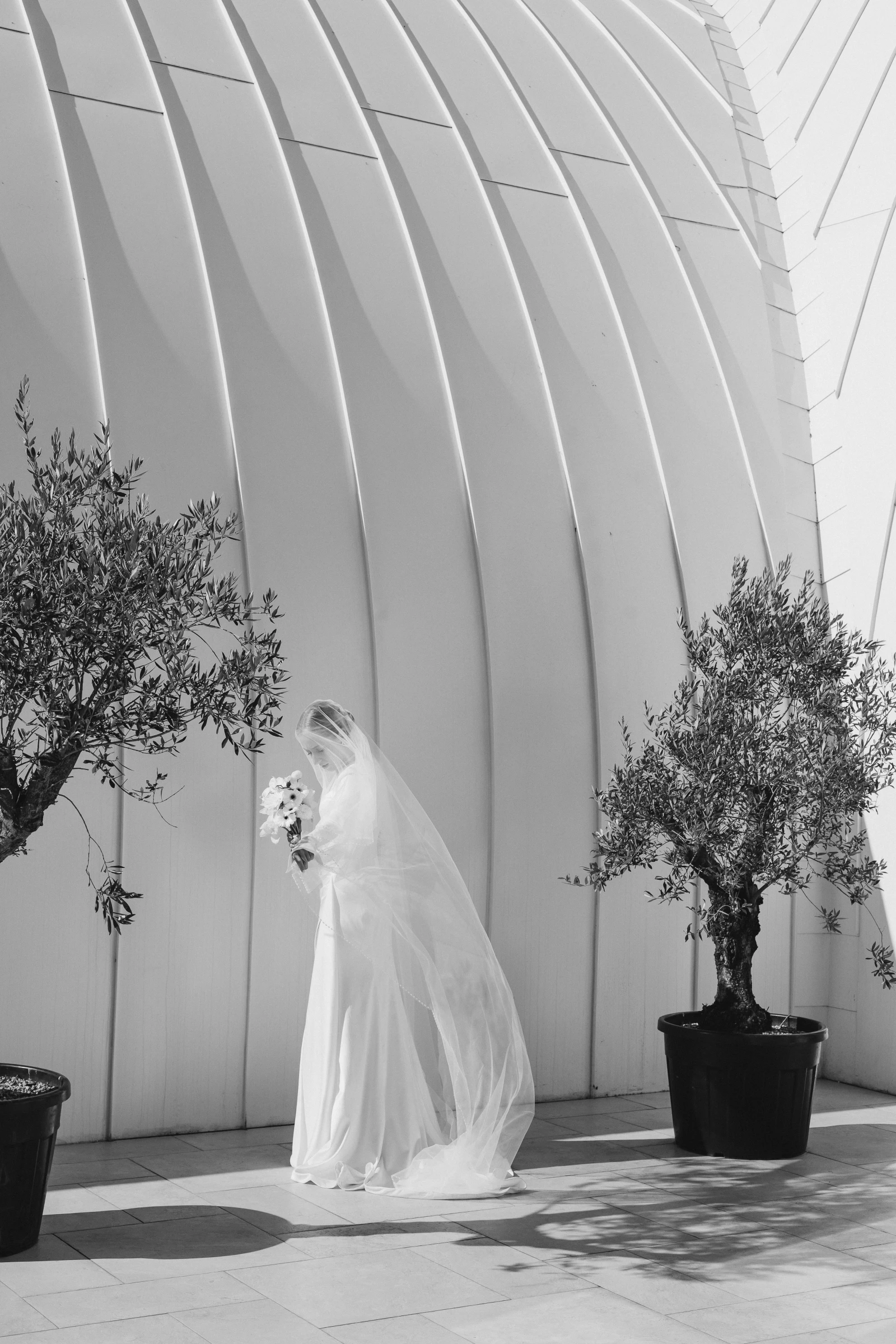 невеста с фатой стоит у стены павильона рядом с деревьями