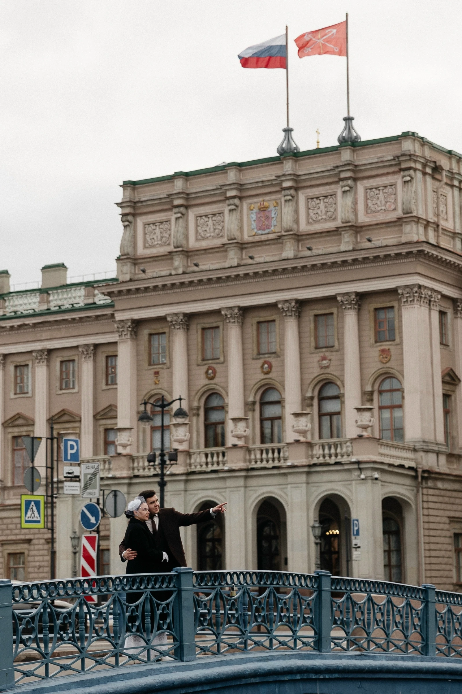 Пара идёт по мосту на фоне здания с флагами города