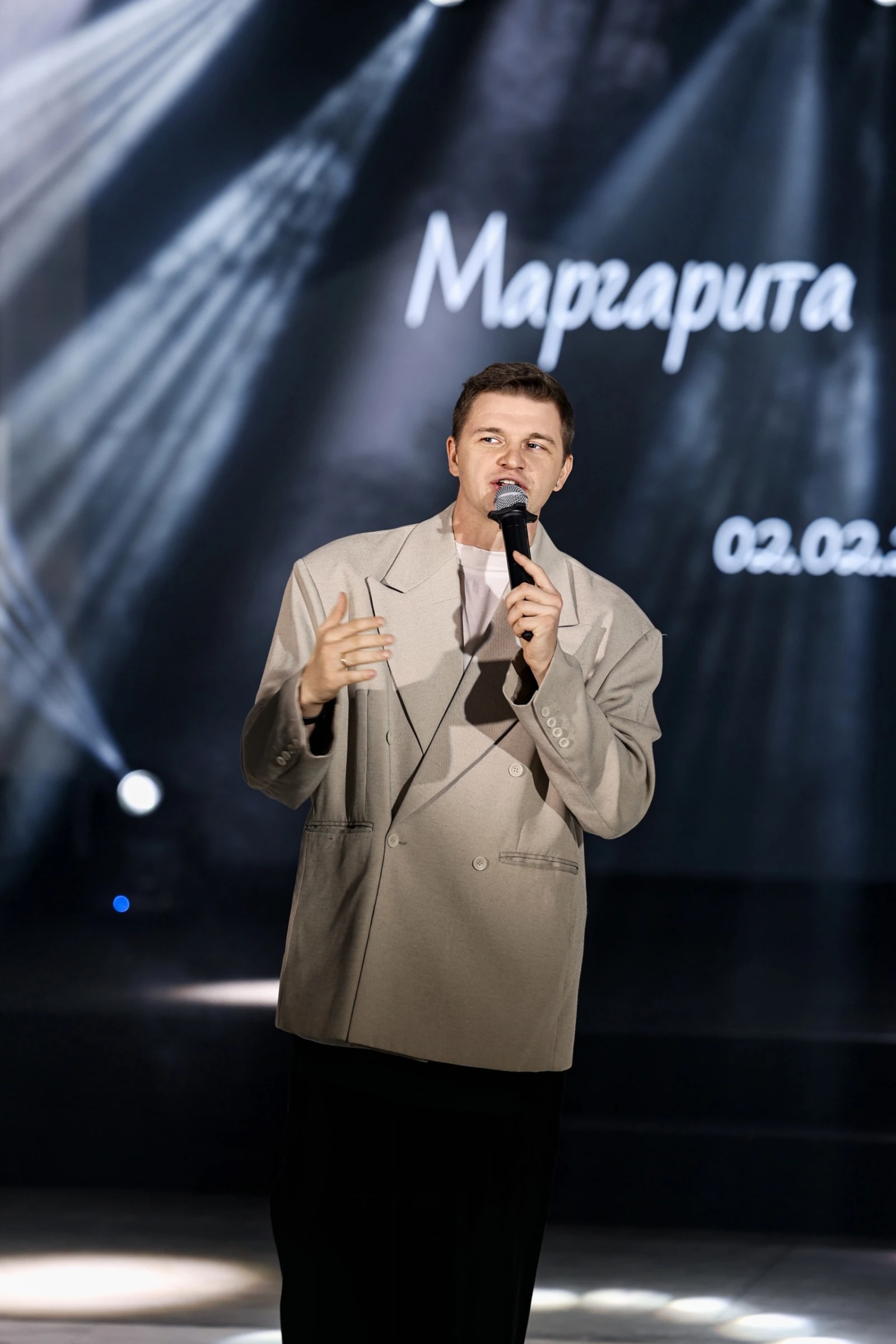 ведущий с микрофоном на сцене на фоне подсветки