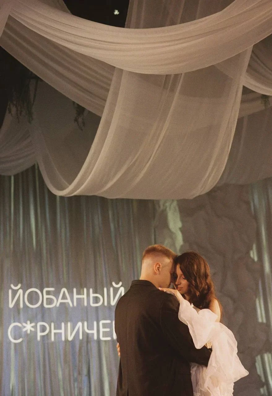 пара обнимается на фоне светящейся надписи под драпировкой
