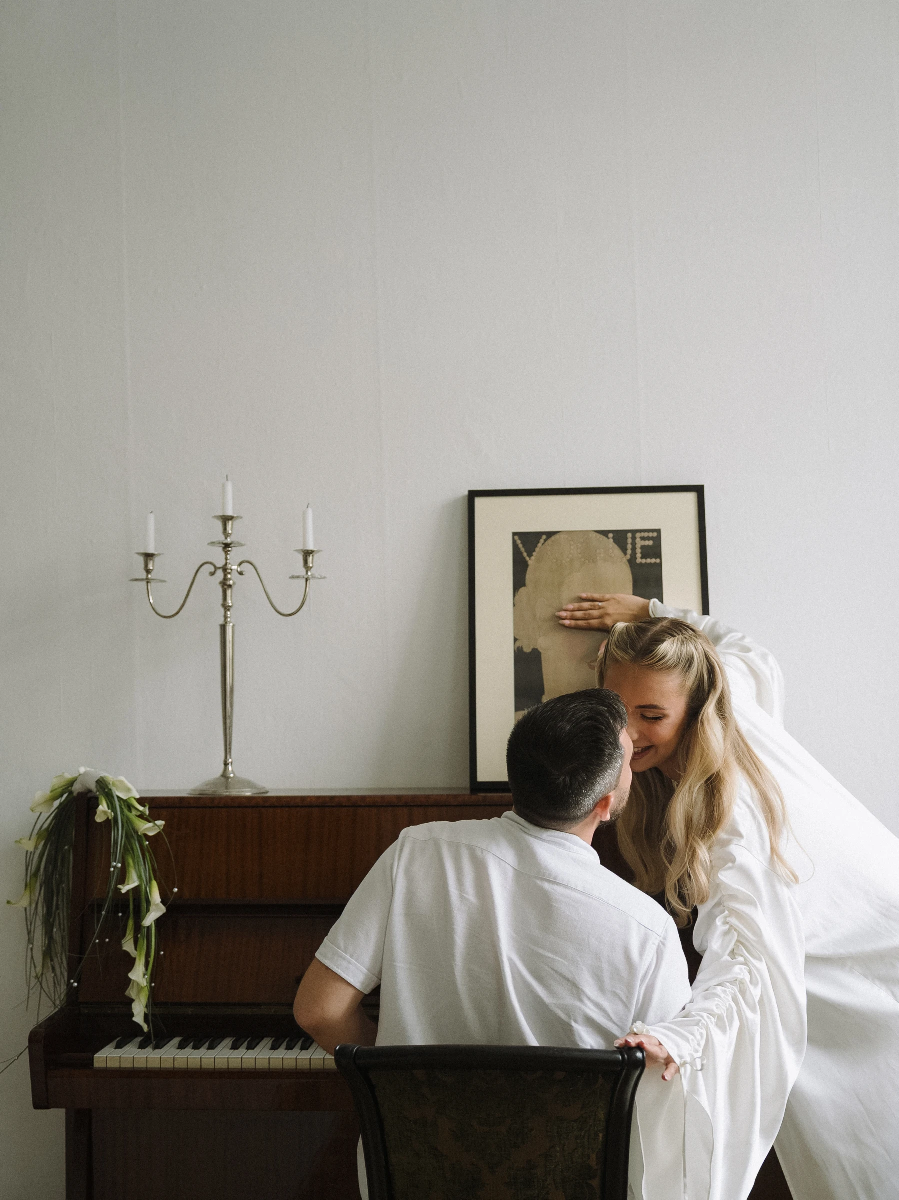 Жених обнимает невесту у пианино в комнате для сборов