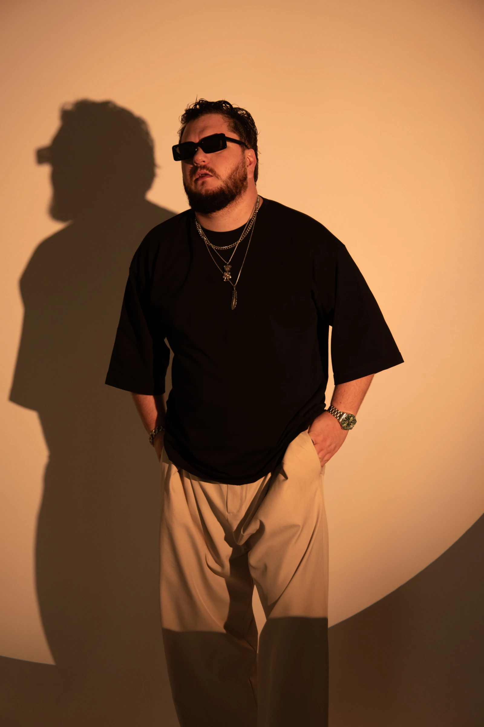 мужчина в очках и цепочках позирует на оранжевом фоне