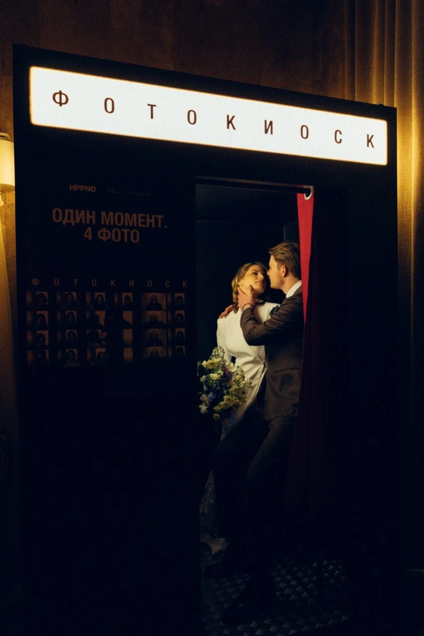 жених и невеста обнимаются у ретро фотокиоска на свадьбе