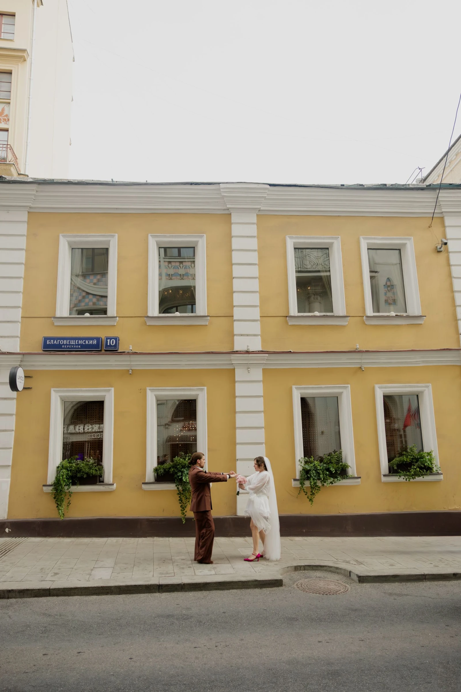 жених и невеста танцуют на улице у жёлтого здания