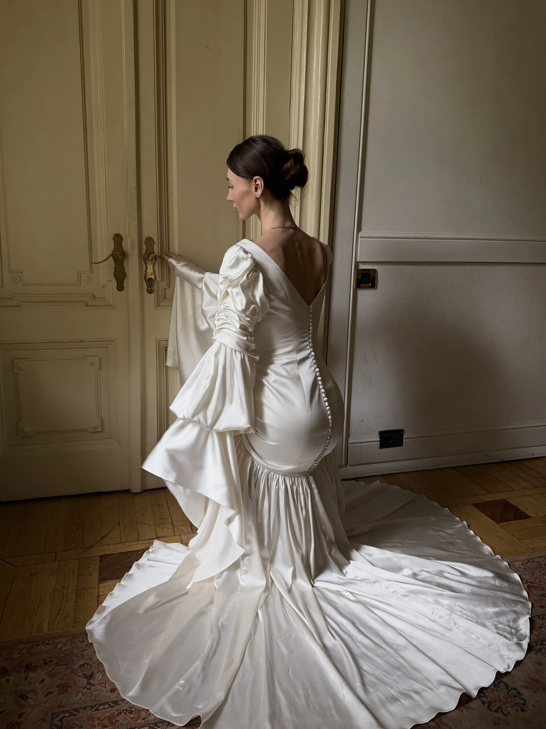 невеста в атласном платье с объёмными рукавами держится за дверь