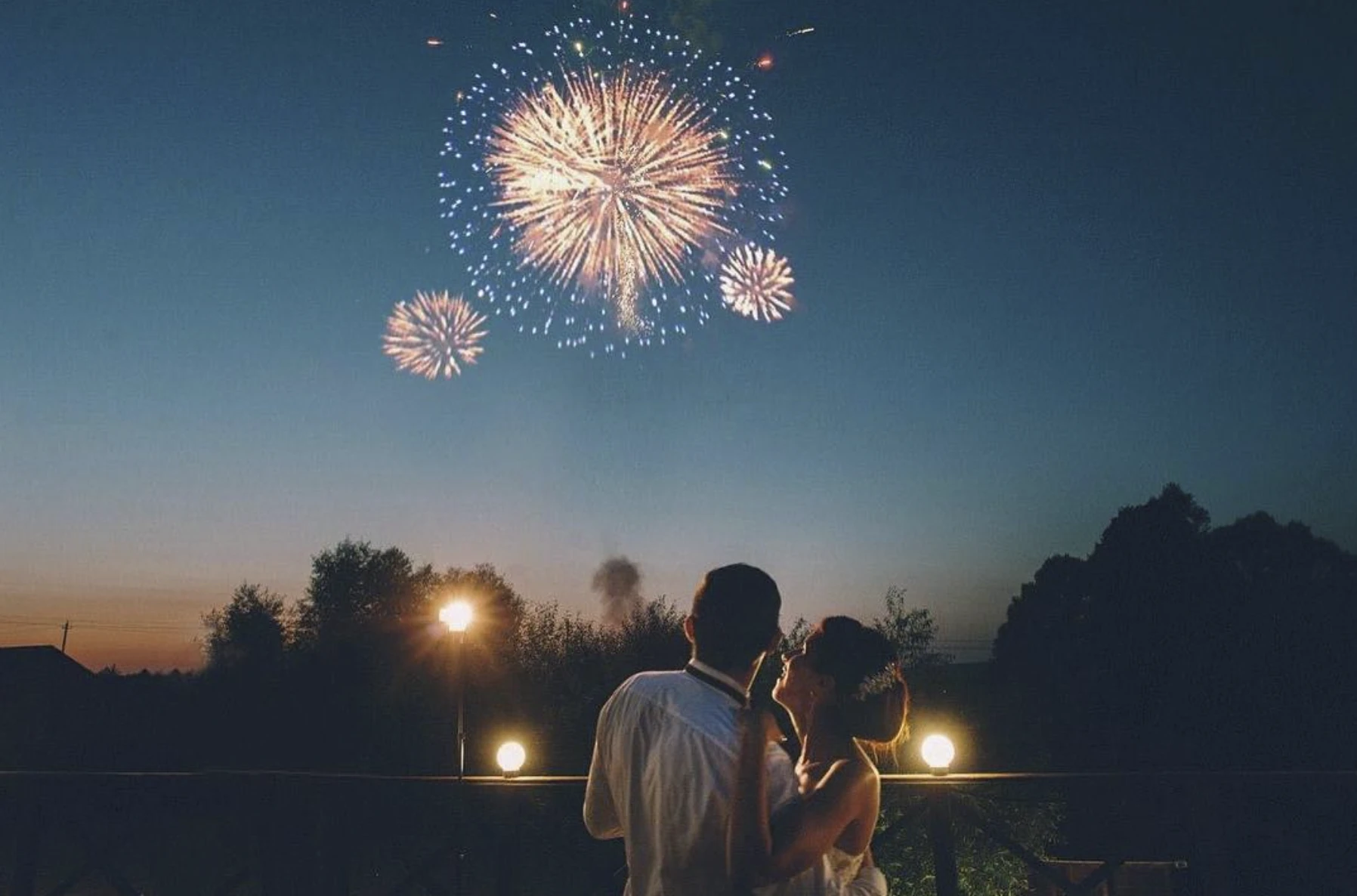 Пара обнимается, глядя на фейерверк в вечернем небе
