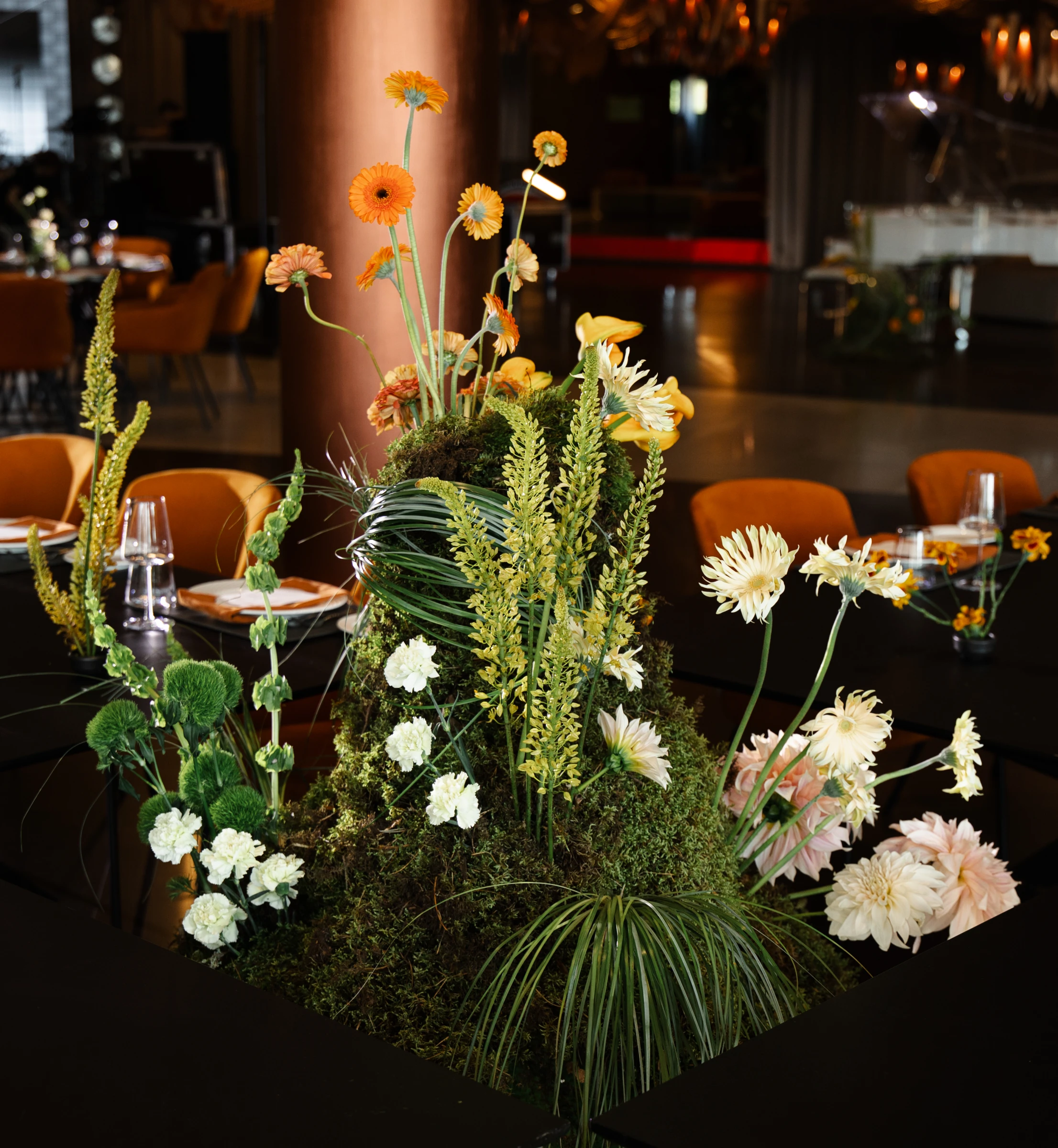 Высокая цветочная композиция из мха, герберы и орхидей на банкетном столе