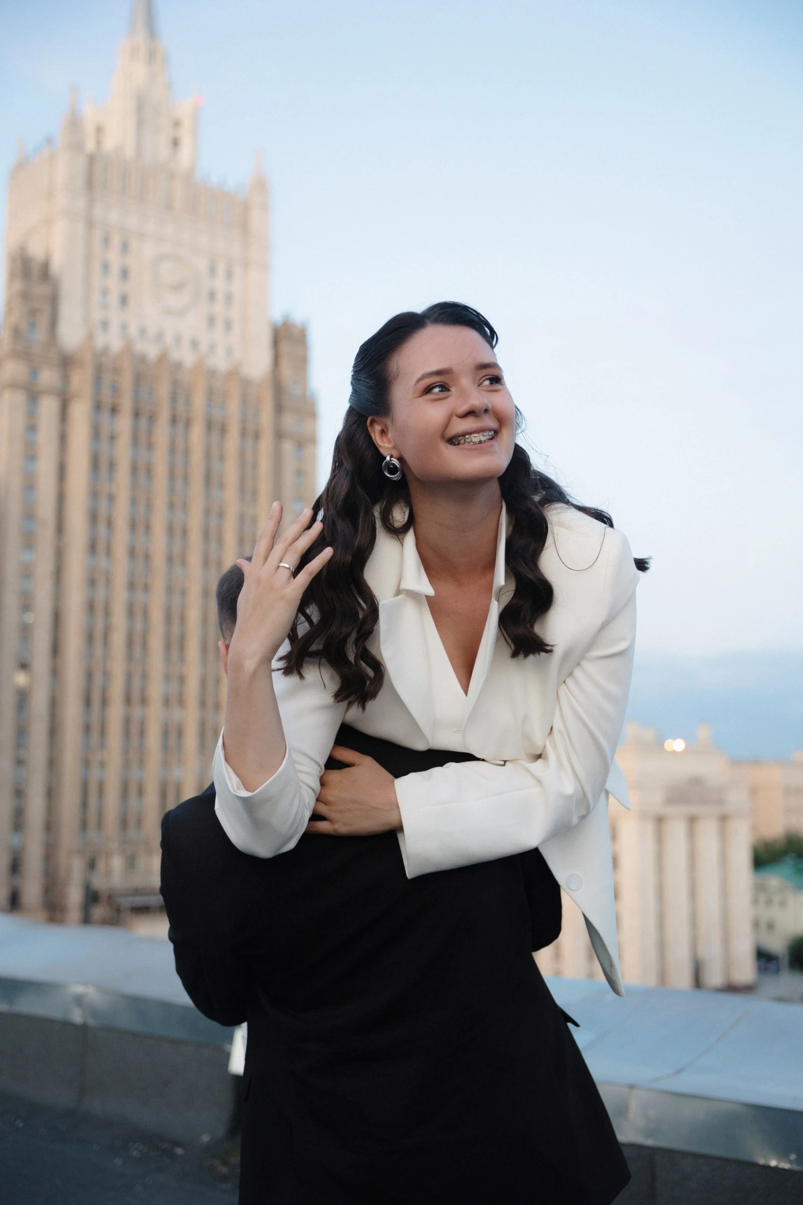 невеста смеется на фоне высотки обнимая жениха на крыше