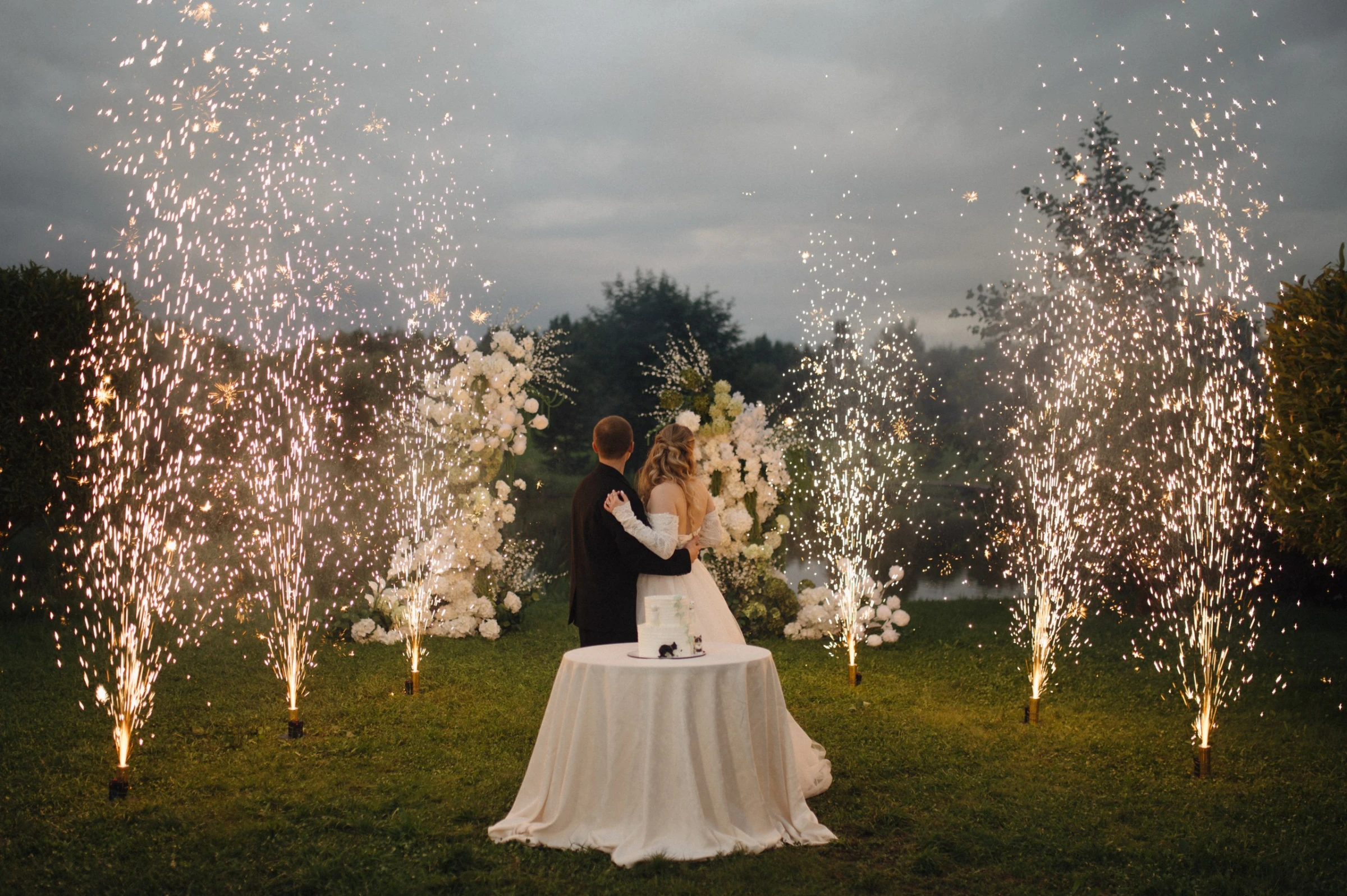 молодожёны танцуют среди фонтанов огней вечером у арки